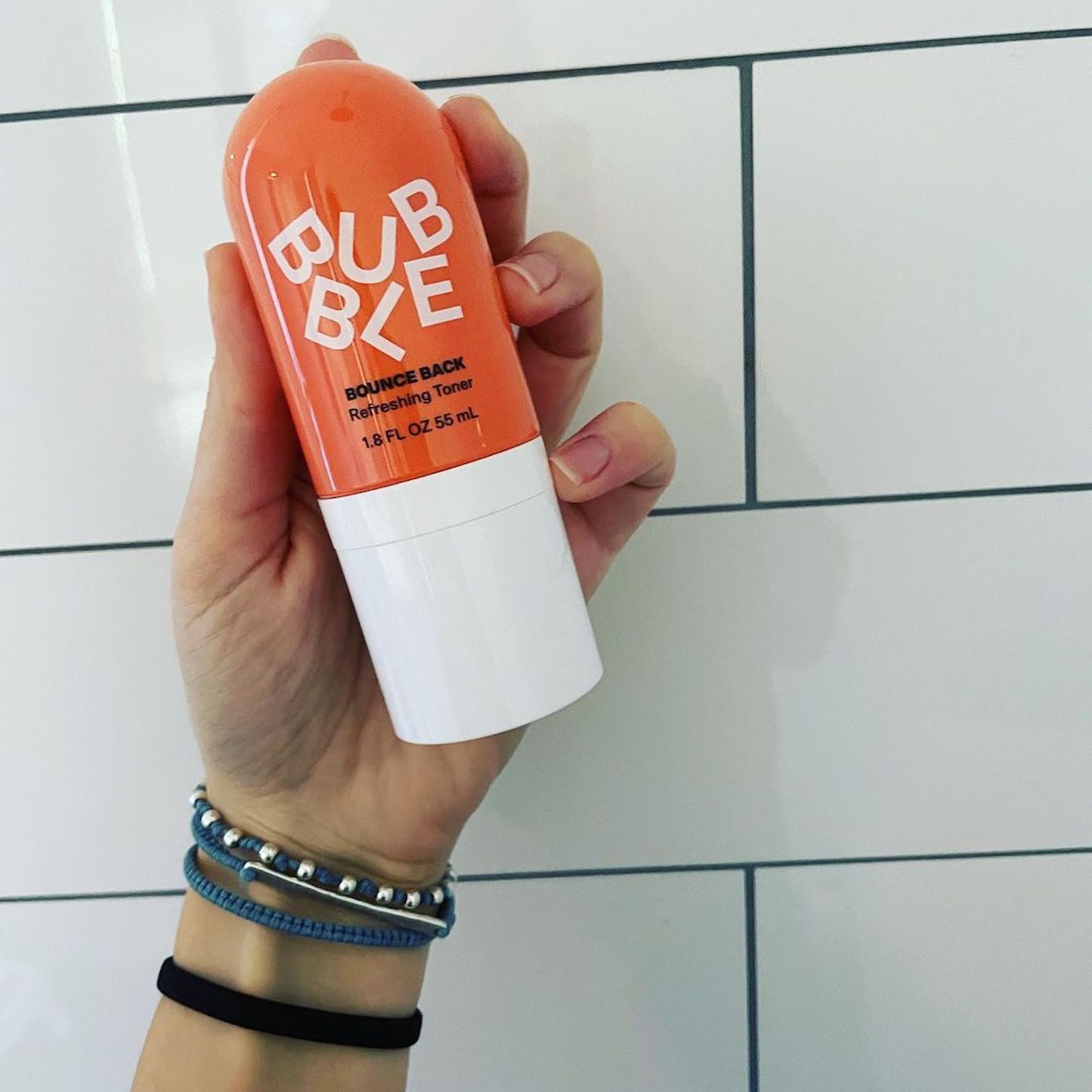 Hand holding Bubble's Bounce Back Refreshing Toner mist against tile background