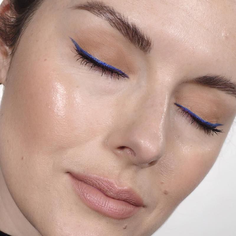 Close-up of Katie Jane Hughes with radiant skin, neutral eyeshadow, and blue winged liner