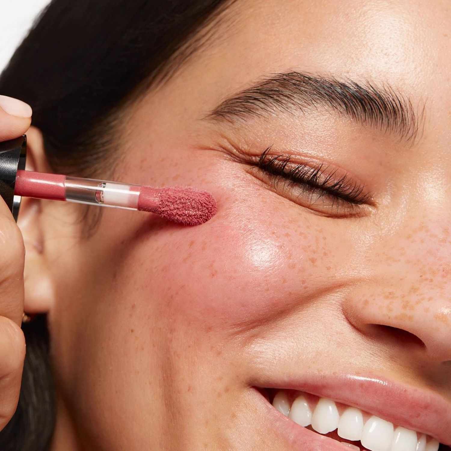 Woman smiling while applying liquid blush to her cheek