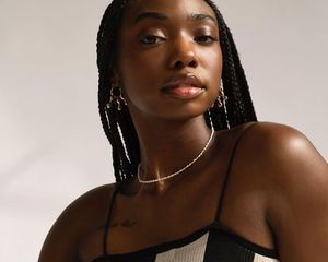 Woman with pearl choker necklace, box braids, gold earrings, and black and white top