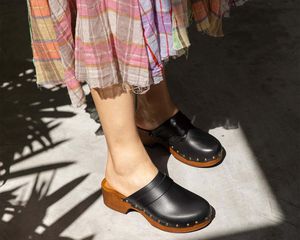 Model wearing black clogs and a plaid skirt.