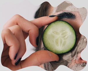 Close up of a woman holding a cucumber to her eye.