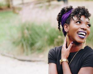 A woman with a purple headband, nailpolish, and lipstick smiling and looking toward the right.