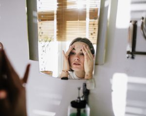 Woman looking in mirror while cupping her face.
