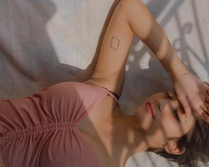 Small square tattoo on arm of girl laying down in pink shirt