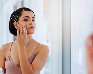 Woman applies moisturizer in front of a mirror