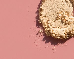 Close up of a crushed yellow powder on a pink background.