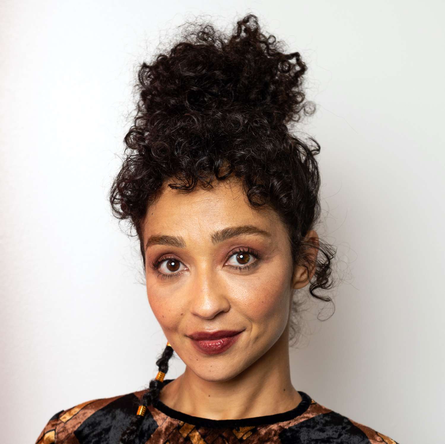 Ruth Negga wears a curly high bun hairstyle with baby bangs