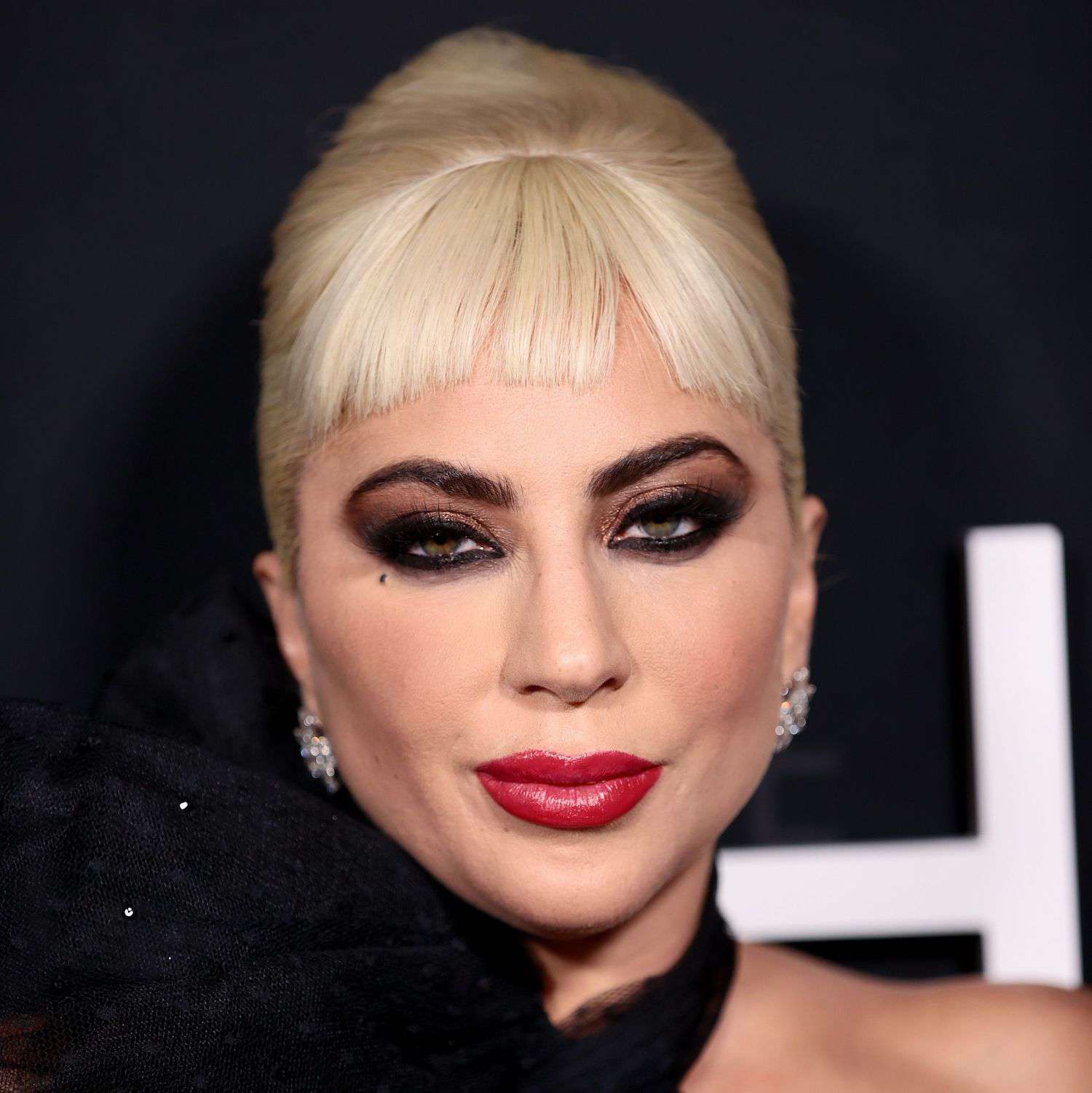 Lady Gaga wears sleek platinum baby bangs, a retro updo, and dramatic eyeshadow