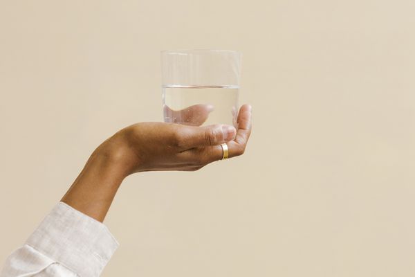 Hand holding a glass of water against a tan background.