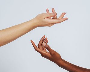 A fair skinned hand and a darker skinned hand against a gray background.
