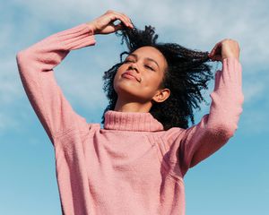 Portrait of young woman against sky touching her hair