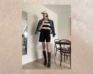 Byrdie writer wears tailored shorts with boots, striped shirt, denim jacket, and cap
