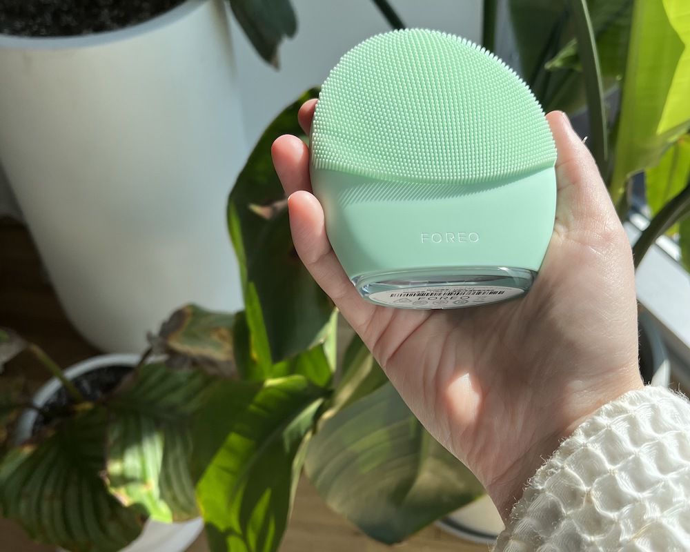 Mint-colored Foreo Luna 4 skincare device in hand with plant in background