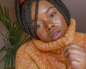 woman with no-makeup makeup in an orange turtleneck and braids