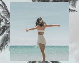 woman standing with her hands extended in front of water on a beach