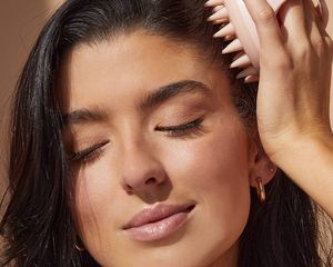 woman with brunette hair rubbing pink scalp massager on head