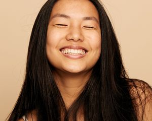 woman with long black hair smiling on a tan background
