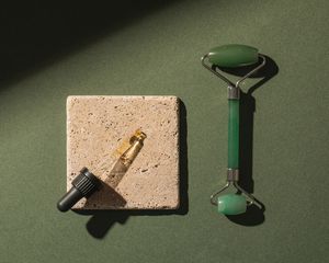 Eye serum in a dropper and a jade roller on a green background