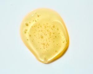 Drop of yellow-toned oil/serum texture on gray background