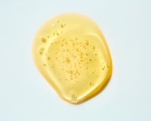 Drop of yellow-toned oil/serum texture on gray background