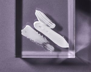 White cream swatches on a clear block, with a purple background.