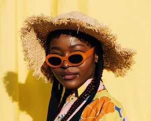 Woman with box braids wearing orange sunglasses and a woven sun hat