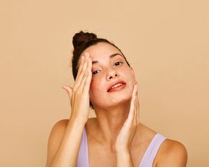 Woman rubs skincare into her face with both hands