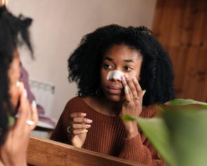 Woman applying pore strip to nose in mirror