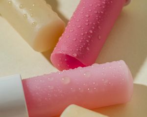 Clear, light pink, and dark pink stick lip balms with water droplets