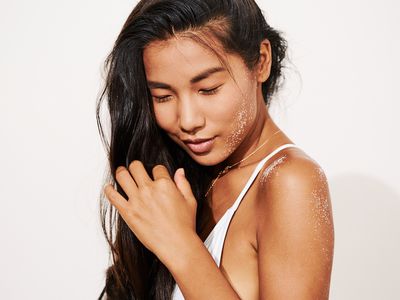 woman combs her fingers through her hair with sand on her shoulder and face