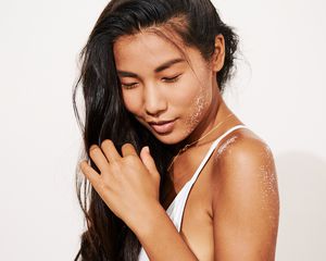 woman combs her fingers through her hair with sand on her shoulder and face