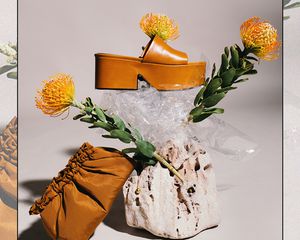 A pair of clogs with a brown purse and yellow flowers