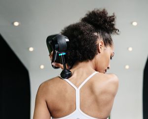 Woman uses a Theragun on her upper back.