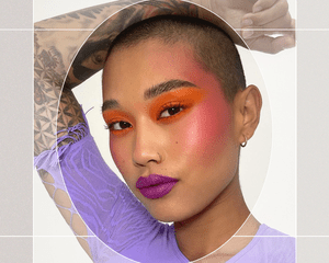 Portrait of AAPI Subject with Buzzcut Wearing Bold Orange Eyeshadow that Blends into Pink Blush Draping and Purple Lipstick