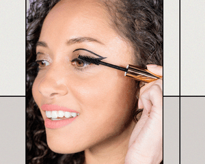 BIPOC Woman Applying Mascara in Addition to her Beige Sparkly Eyeshadow and Graphic Eyeliner